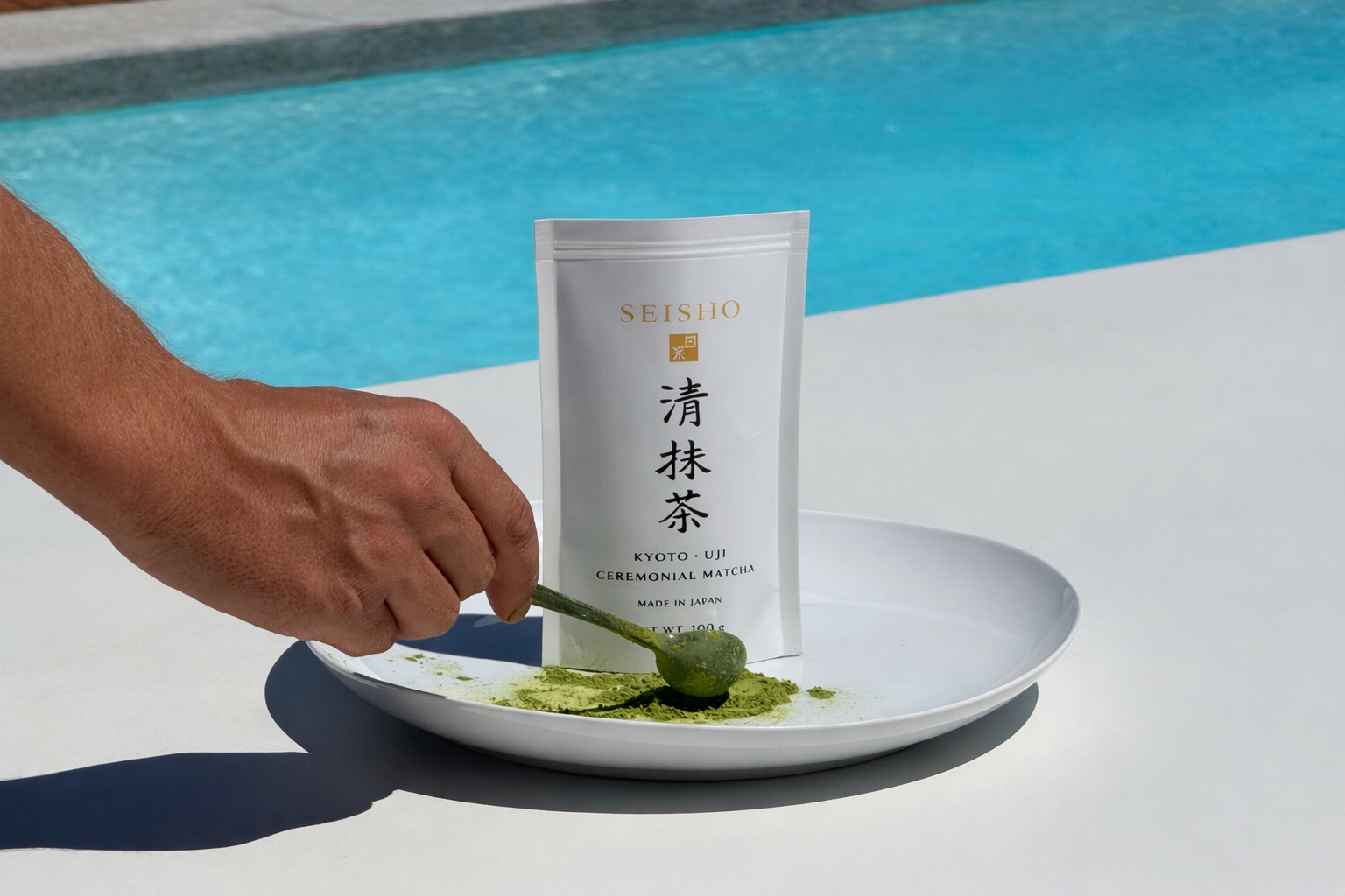Seisho Ceremonial Matcha Beutel auf einem Teller am Pool, während eine Hand feines Matcha-Pulver mit einem Löffel portioniert.